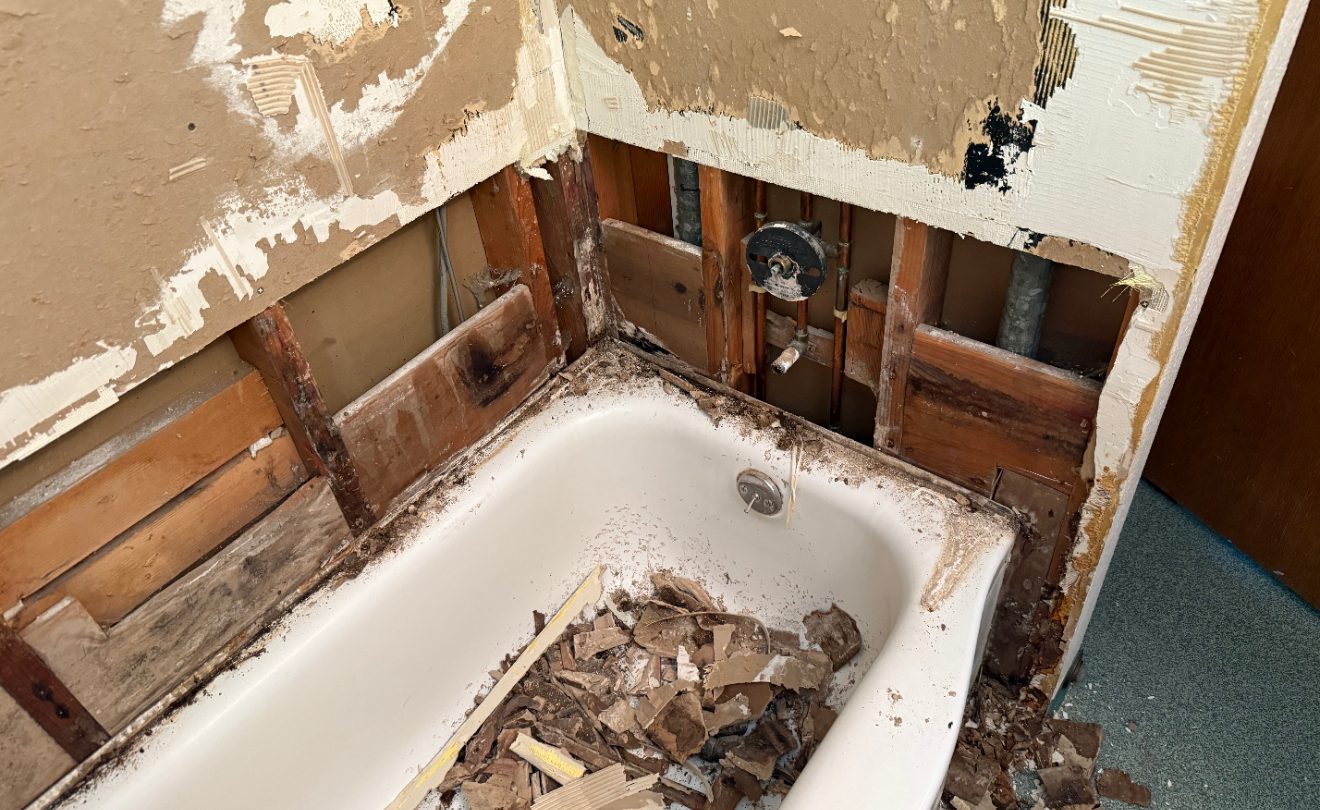 Bathtub wall opened to the studs, showing water-damaged framing behind the old tub surround